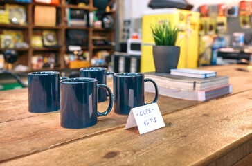 Close up of breakfast blue mugs over wooden counter in local store with industrial style decoration. Interior of empty retro shop with discount articles on table. Small business concept. No People.