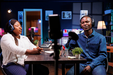 African American content creator couple talks tech in their home studio, entertaining a wide online...
