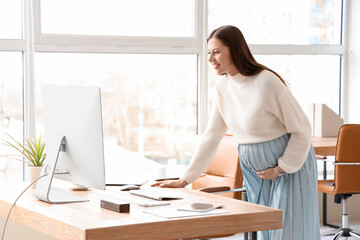 Young pregnant businesswoman working at table in office