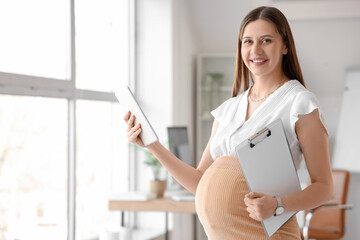 Young pregnant businesswoman with tablet computer and clipboard in office