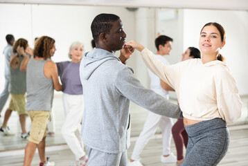 Positive young girl and adult African American man dancing as couple during group class in dance...