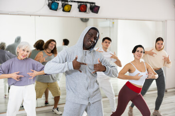 Fototapeta na wymiar Energetic African American man practicing hip-hop movements during adult group dance class in studio