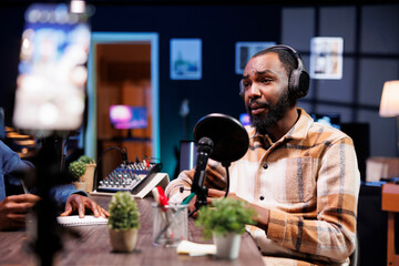 African American influencer in the studio, using a high-tech microphone for an internet program on a livestreaming channel. Man doing a podcasting session with quality streaming recording equipment.