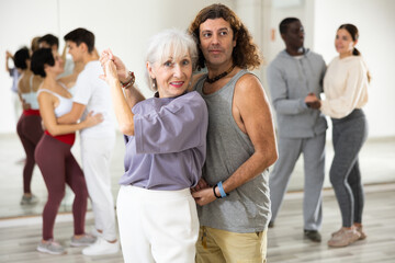 Smiling mature woman and man attending group choreography class, learning modern pair dances. Concept of active lifestyle..