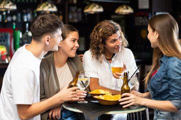 Group of friends standing at table in bar, drinking beer and having conversation.