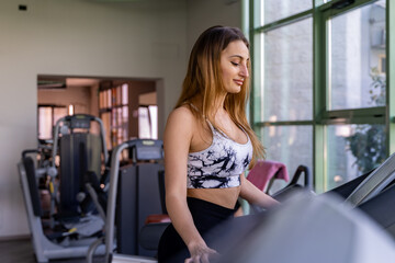 Fototapeta na wymiar young blond woman running in sportswear on the treadmill in a gym