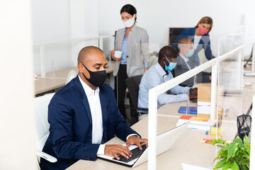 Portrait of busy hispanic entrepreneur in protective face mask working with laptop in coworking...