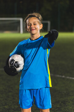 a young girl in a blue soccer uniform holding a ball and pointing to the camera, medium shot, soccer practice. High quality photo