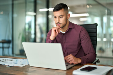 Busy Latin business man working on laptop sitting at office desk. Professional businessman company...