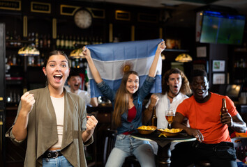 Emotional diverse soccer supporters holding the flag of Argentina and enjoing beer and potato...