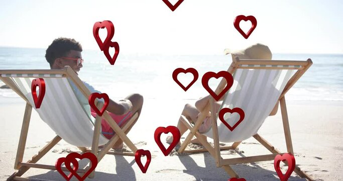 Animation of hearts moving over diverse couple in love in deckchairs on beach in summer