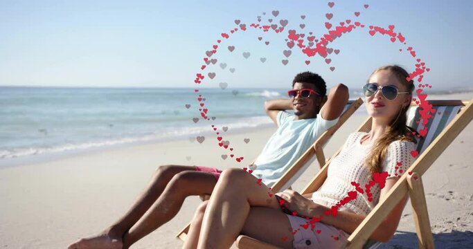 Animation of hearts moving over diverse couple in love in deckchairs on beach in summer