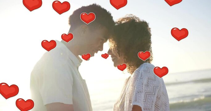 Animation of hearts moving over diverse couple in love touching heads on beach in summer