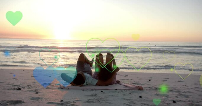 Animation of hearts moving over diverse couple in love lying on beach in summer