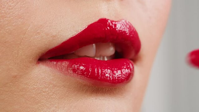 Young woman make-Up with a Red Lipstick on her lips close-up. Shooting of woman applying red lipstick. Make up routine, pink background