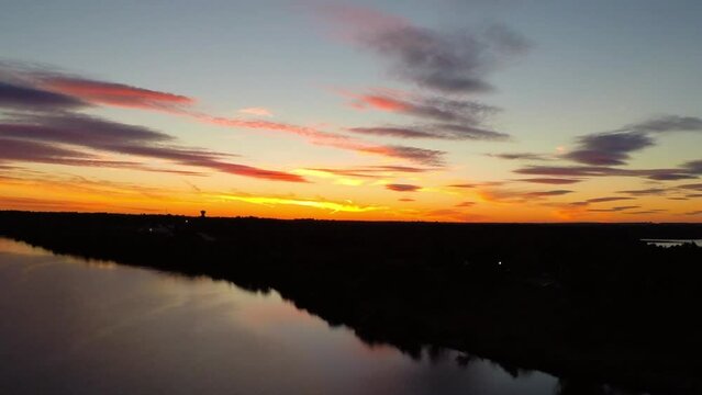 Aerial Forward Ascending Shot Of Reflection Of Trees In Rippled River Under Orange Cloudy Sky At Sunset - Buckner, California