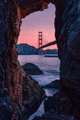 A view of the Golden Gate Bridge from inside, framed by two rocks on both sides, with a pink sky in...