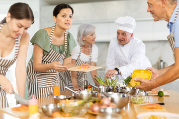 Chef in cook uniform teaches cooking class students how to clean and cut salmon fillet