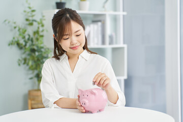 Obraz na płótnie Canvas 豚の貯金箱にお金を入れる女性