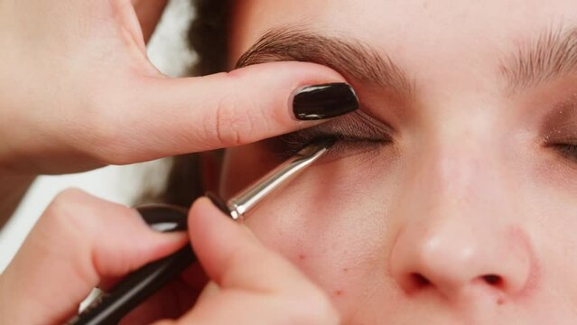 Eye shadow makeup to the upper eyelid, close-up. Makeup artist applies a bright eye shadow with a make-up brush.Tutorial master class of professional makeup, smoky eyes 
