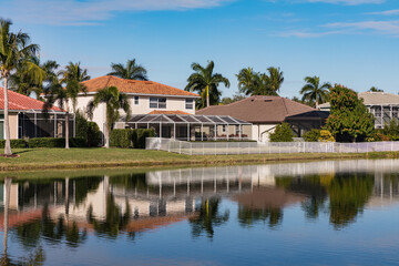 Fototapeta na wymiar Typical concrete house on the shore of a lake in southwest Florida in the countryside with palm trees, tropical plants and flowers, lawn and pine trees. Florida.