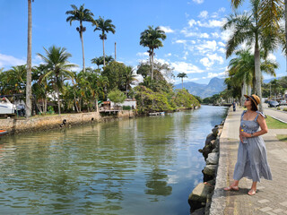 Fototapeta na wymiar Woman in long dress on sidewalk along river with palm trees