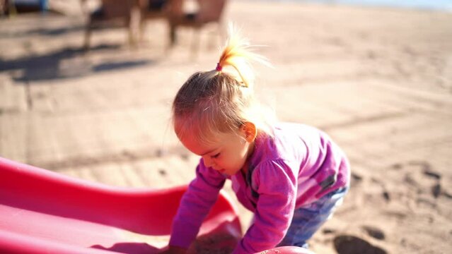 Little girl pours sand on a slide on the beach and wipes it off. High quality 4k footage