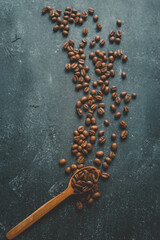 Coffee beans pour out from a wooden spoon on a retro background, top view