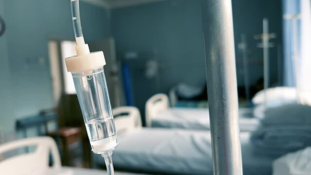 Drip chamber in an IV hangs on a medical infusion stand against the background of blurred medical beds in a clinic ward. Intravenous injections, medical care. Recovering patient in a hospital. Closeup