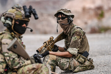 Fototapeta premium Soldiers in camo gear during a tactical operation with binoculars and rifles on a rocky terrain, showcasing military precision and readiness.
