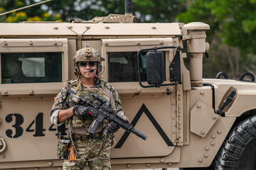 Confident soldier in full gear stands before a military vehicle, rifle in hand, showcasing...