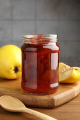 Tasty homemade quince jam in jar and fruits on wooden table