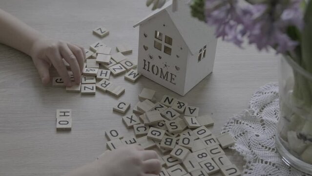 small child 4 years old playing with wooden alphabet blocks, makes up word home from letters, house model, concept home mortgage, home insurance, exploring English language