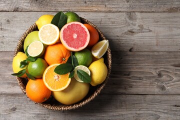 Different fresh citrus fruits and leaves in wicker basket on wooden table, top view. Space for text - 764411056