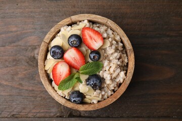 Fototapeta na wymiar Tasty oatmeal with strawberries, blueberries and almond flakes in bowl on wooden table, top view