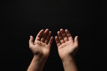 Religion. Man with open palms praying on black background, closeup