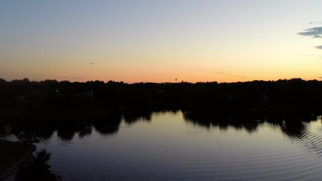 Aerial Backward Shot Of Rippled Pattern In Tranquil River Amidst Trees On Landscape Against Orange Sky During Sunset - Buckner, California