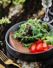 Beef tongue salad with rucola, avocado, cherry tomatoes and sauce on plate on marble background with drinks. Healthy food, close up