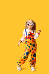 Playful little girl in clown costume with funny glasses on yellow background