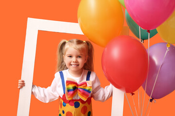 Fototapeta na wymiar Cute little girl in clown costume with balloons and frame on orange background