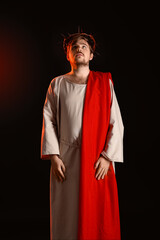 Man in Jesus robe and crown of thorns with red light on black background