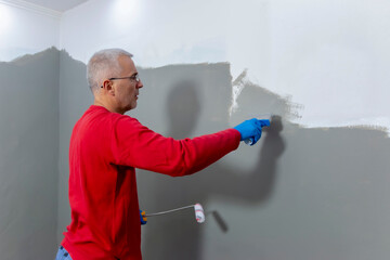 A builder worker applying waterproofing paint to the bathroom wall and floor. Applying...