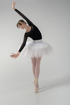 ballerina in a black bodysuit and tutu poses in motion showing ballet elements while standing on pointe shoes