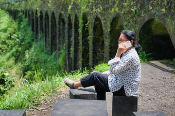 Woman sitting alone on concrete block, making a phone call from the park