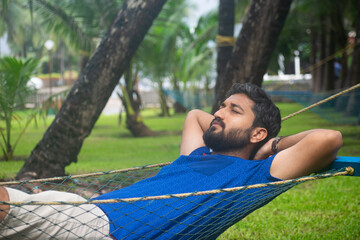 Picture of an Indian person smiling and resting on a hammock at a beach resort. resorts, hotels,...