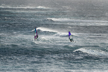 The silhouette of two Windsurfers in rough waves. 