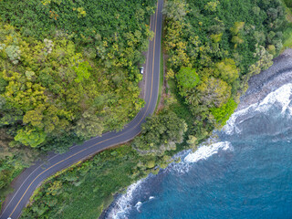An aerial view of a winding road along a lush tropical coastline with crystal clear turquoise...
