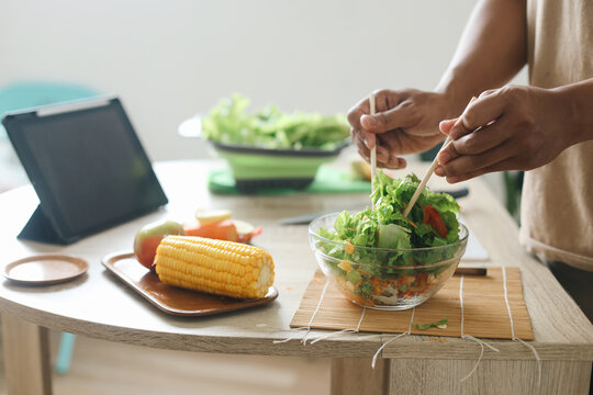 Man making salad with fresh vegetables while watching online culinary class on tablet 