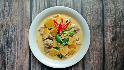Red curry chicken with pumpkin and coconut milk in white bowl on wooden table. Authentic Thai food.