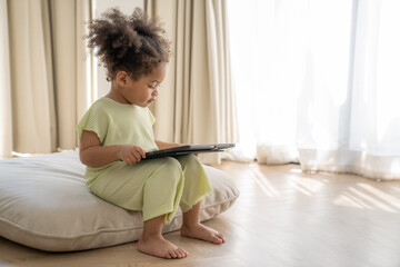 African American little girl playing and using a tablet at home - 764461482